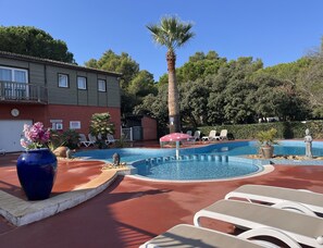 A pool area with lounge chairs, a palm tree, and a building with a balcony.
