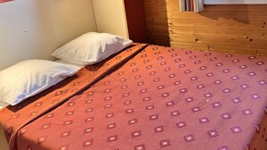 A single bed with a patterned bedspread, a headboard, and a window with curtains.