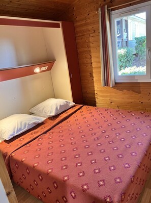A single bed with a patterned bedspread, a headboard, and a window with curtains.