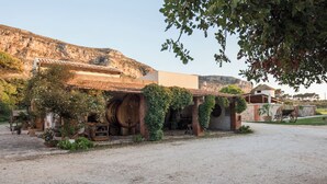A rustic building with a large barrel, a wheelbarrow, and a stone wall. - Agriturismo Tenuta Pizzolungo (Erice)