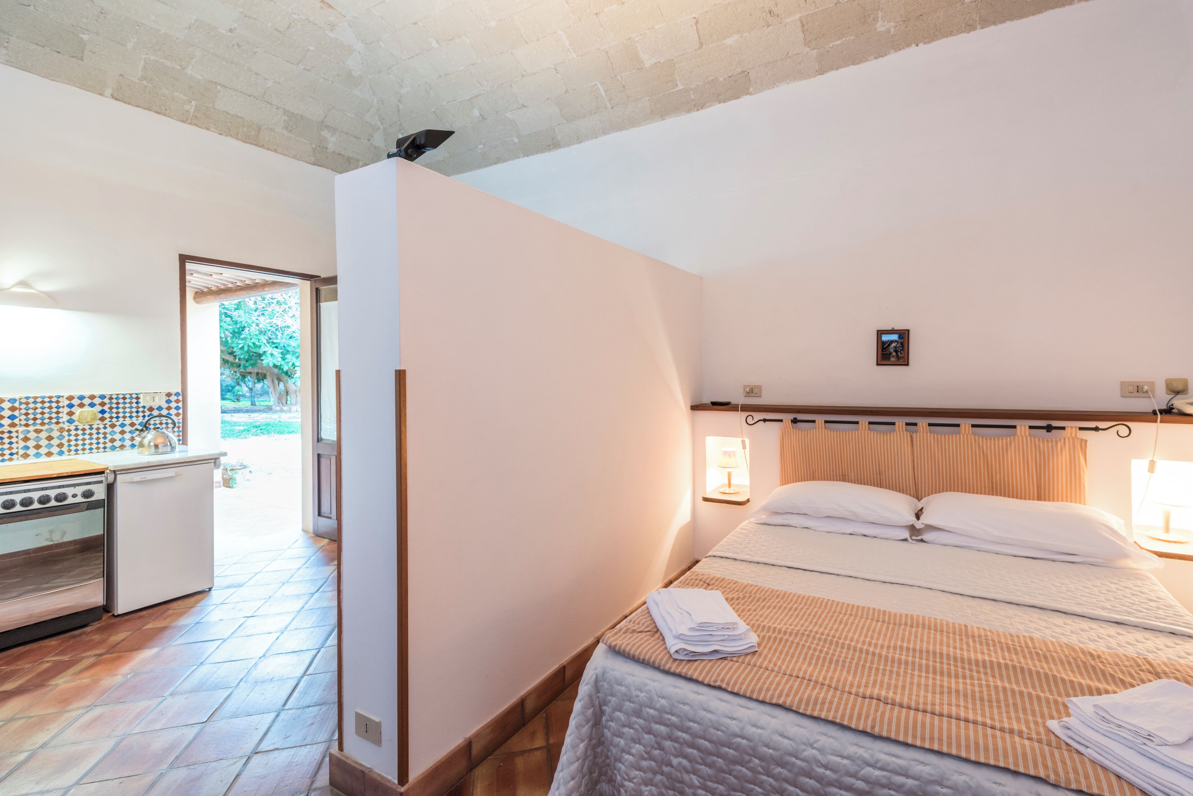 Quarto com cama, mesa de cabeceira pequena, janela e vista para o exterior.