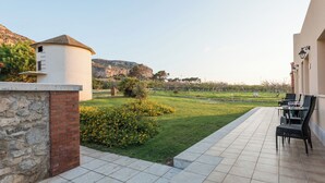A patio with outdoor furniture, a stone wall, and a grassy area with a view of a mountain. - Agriturismo Tenuta Pizzolungo (Erice)