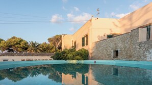 A swimming pool with a stone wall and a building with a tiled roof in the background. - Agriturismo Tenuta Pizzolungo (Erice)