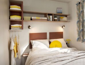 A bedroom with a bed, bedside tables, a wardrobe, and a shelf with folded towels and books. - Comfortable Coastal Stay for 4 (Hyères)