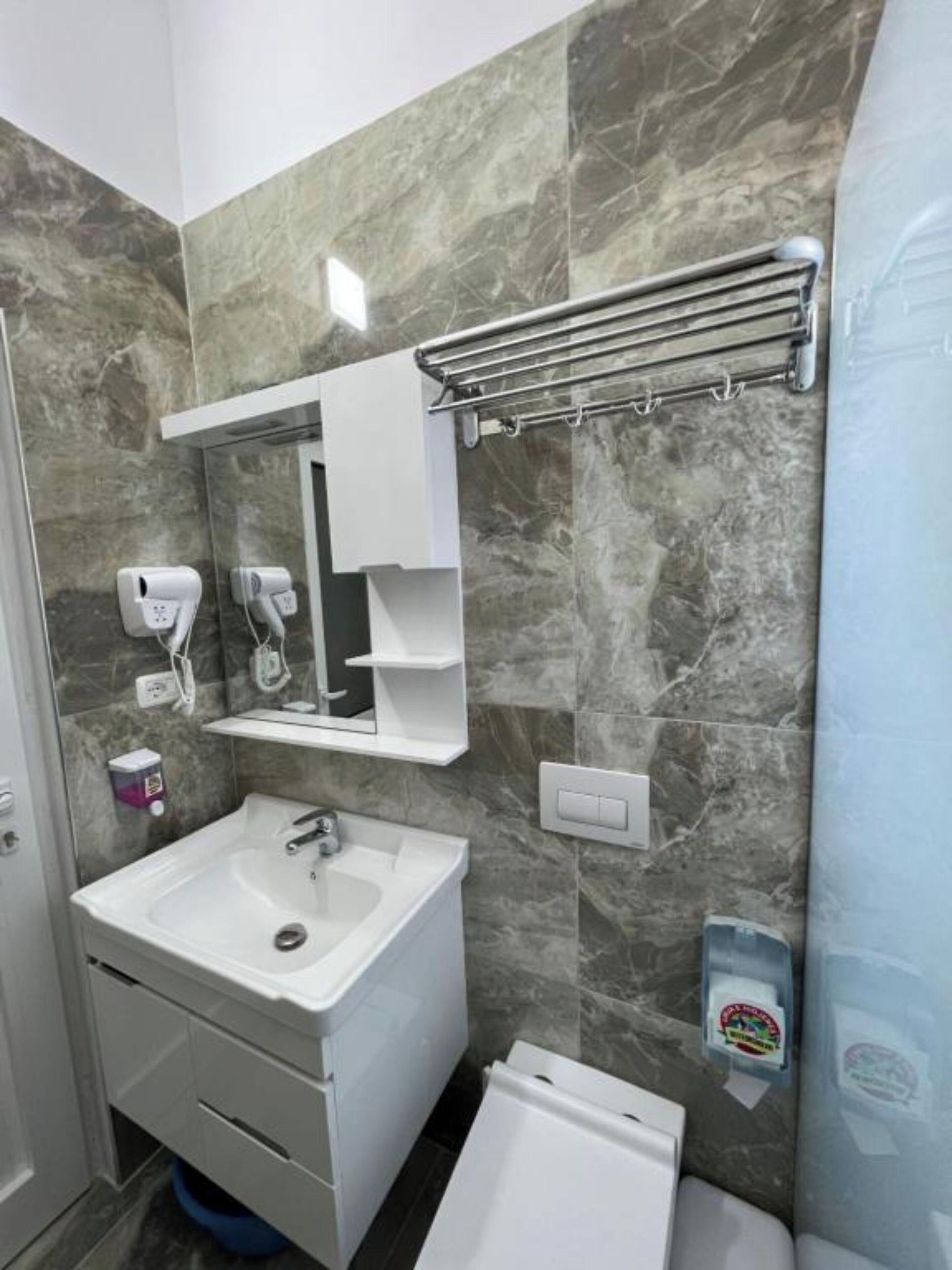 Un baño con lavamanos, espejo, toallero y dispensador de jabón.