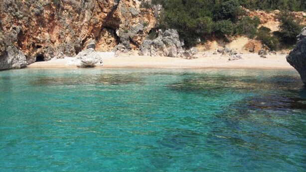 Eine Küstenansicht mit klarem türkisblauem Wasser, einem Sandstrand und felsigen Klippen.