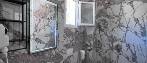 A bathroom with a marble wall, a sink, a toilet, and a framed picture.
