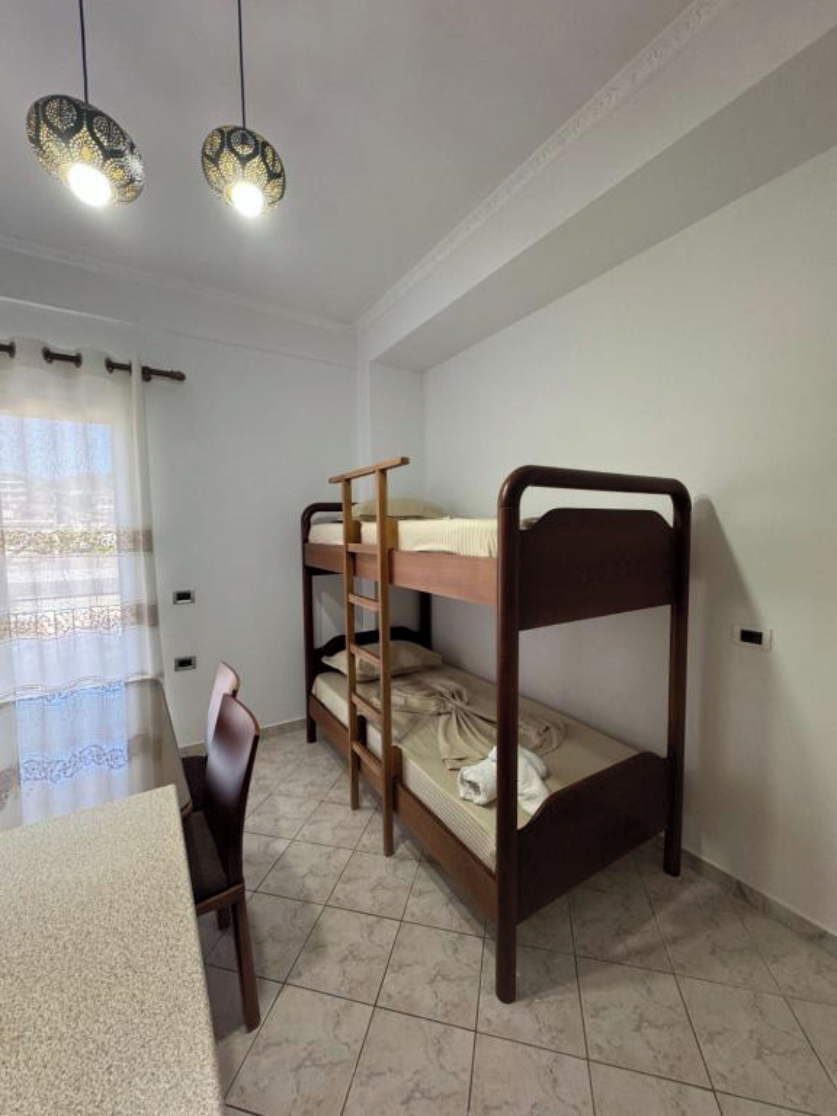 A bunk bed room with a desk and chair, a window with curtains, and two hanging lamps.