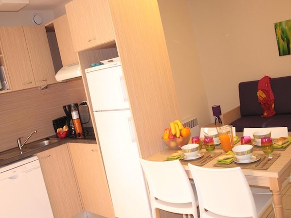 Een kleine keuken met een koelkast, een eettafel gedekt met borden, glazen en een schaal fruit.