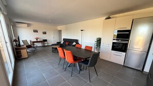 Eine moderne Küche mit grauen Fliesen, einem Esstisch mit orangefarbenen Stühlen, einem schwarzen Sofa und einem Edelstahlkühlschrank.