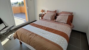 Ein Schlafzimmer mit Bett, Nachttisch, Lampe und Blick ins Freie.