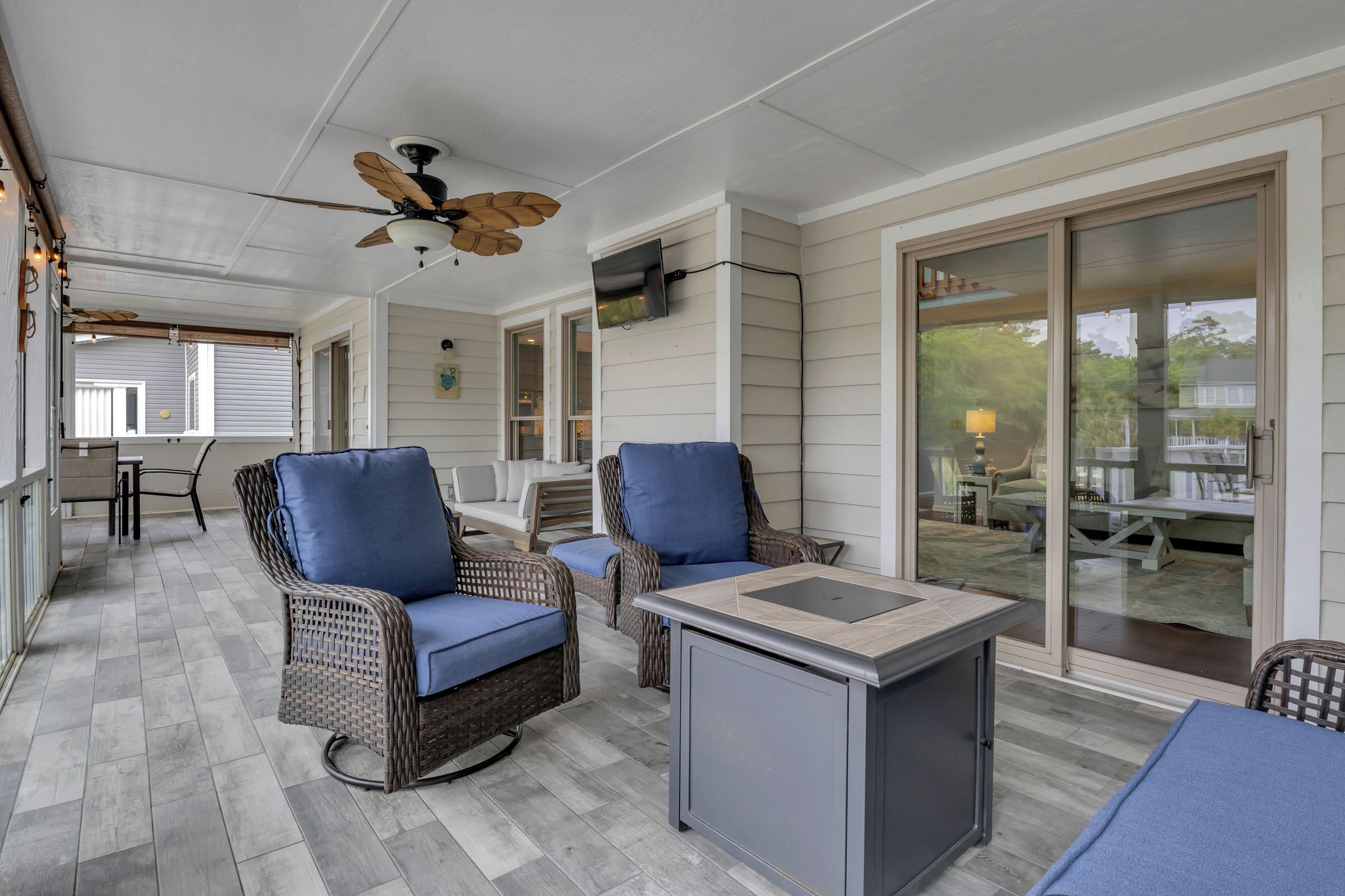 Un patio cubierto con muebles de mimbre, un ventilador de techo y un portón corredizo que da a un espacio al aire libre.