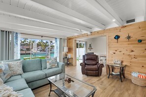 Ein geräumiger Wohnbereich mit einer Holzwand, einem Ledersessel, einem Glastisch und Blick auf einen Pool.