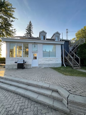 A small, single-story building with a front door, a small porch, and a set of stairs leading to a second-floor balcony.