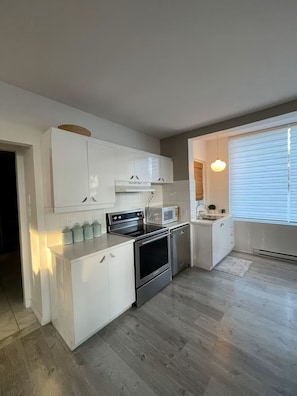 A compact kitchen with white cabinetry, a built-in oven, microwave, and a sink.
