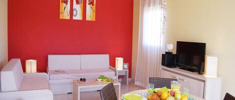 Una sala de estar con un sofá, una mesa de comedor dispuesta con platos y vasos, y un televisor.