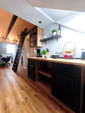 A kitchen with wooden cabinets, a black countertop, a ladder, a coffee maker, and a fruit basket. - North Sea Dreams Scheper - Dune Oasis (Jever)