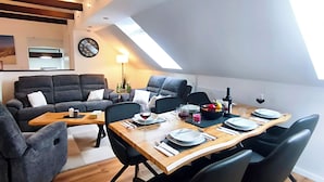 A dining area with a wooden table set for four, surrounded by black chairs, in a loft-style room with exposed beams and a skylight. - North Sea Dreams Scheper - Dune Oasis (Jever)