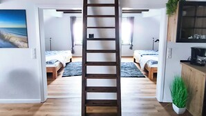 A loft-style room with a central wooden ladder, two beds, a kitchenette, and a view of the beach. - North Sea Dreams Scheper - Dune Oasis (Jever)