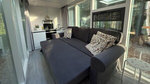 A modern living room with a sofa, a dining area, and large windows. - The Spruce Bliss Pod (Lac du Bonnet)
