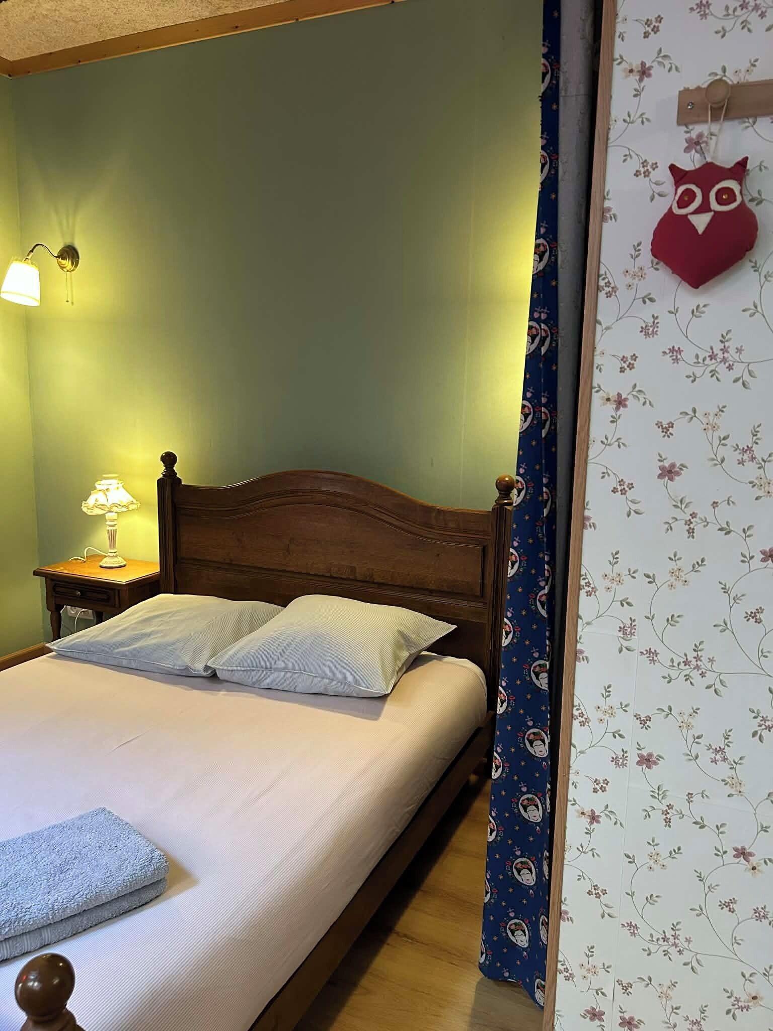 A bed with a wooden headboard, a nightstand with a lamp, and a floral-patterned curtain.