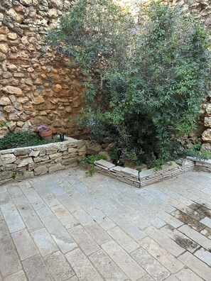 A stone wall, a small tree, and a paved patio area. - L'Amandine - Renovated barn with Jacuzzi (Puisserguier)