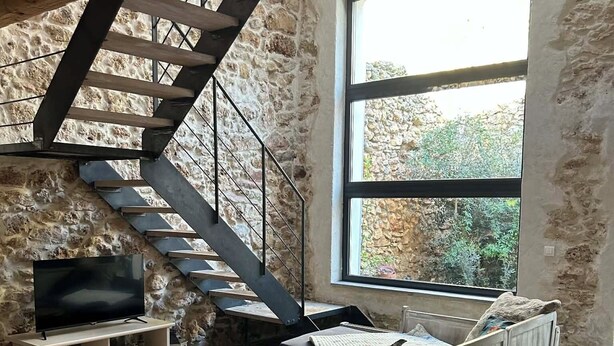 Un salon moderne avec un canapé en bois, une table basse, un téléviseur, un mur en pierre et un escalier.
