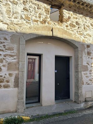 A stone building with a large arched doorway, a smaller door, and a window. - L'Amandine - Renovated barn with Jacuzzi (Puisserguier)