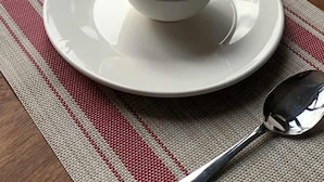 Ruokailuun valmisteltu pöytä, jossa on lautanen, kulho, haarukka ja lusikka alustalla, ja ikkunasta avautuu näkymä kaupunkimaisemaan.