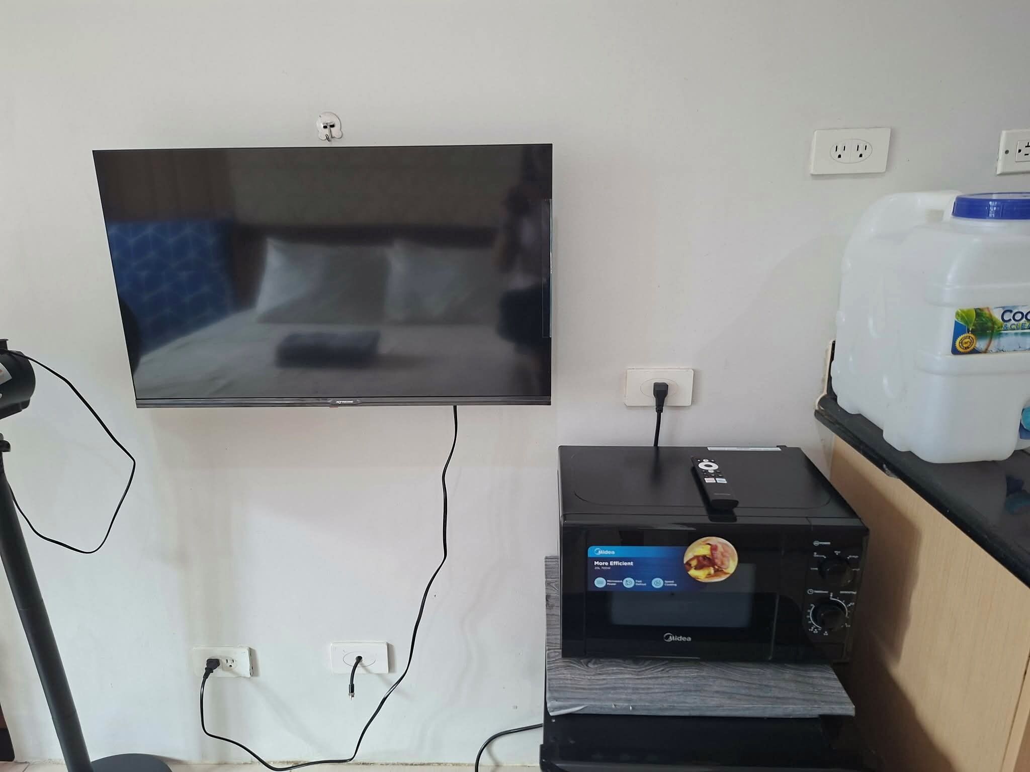 A television mounted on a wall, a small appliance with a control panel, and a white container on a counter.
