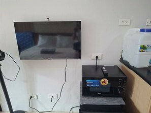 A television mounted on a wall, a small appliance with a control panel, and a white container on a counter. - Cozy High-Rise Haven (Quezon City)