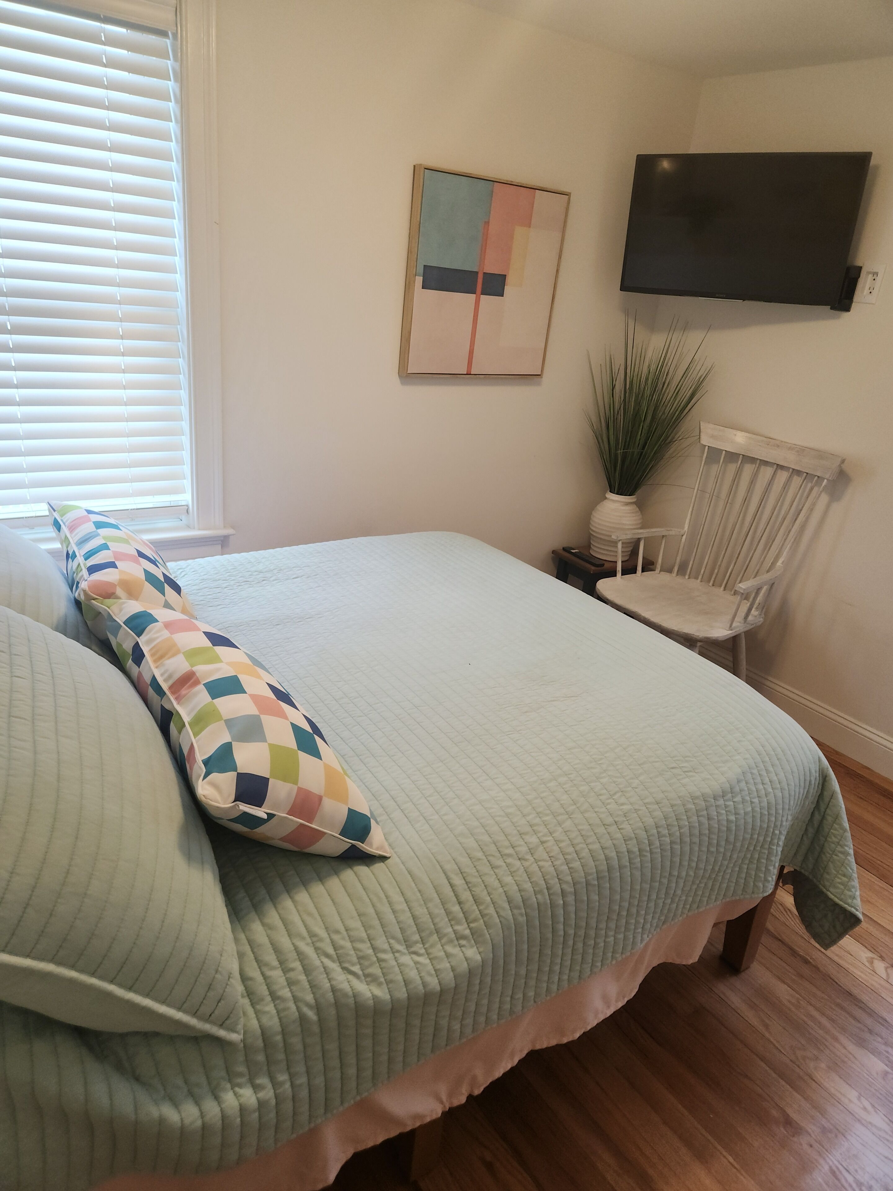 A bedroom with a bed, a chair, a TV, and a painting on the wall.