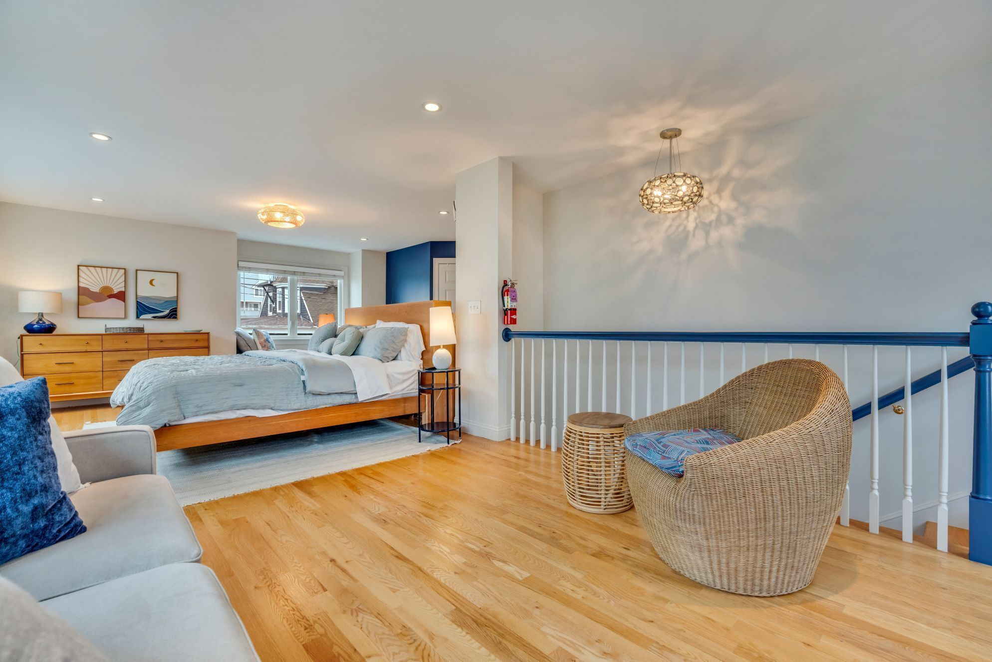 Een moderne slaapkamer met een bed, nachtkastjes, een kast, een rieten stoel en een trap.