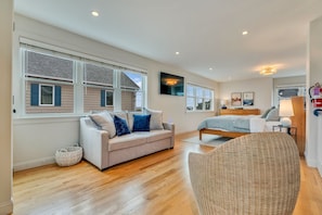 A spacious room with a large window, a sofa, a bed, and a wicker chair.