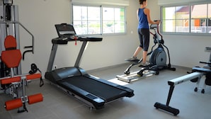 A gym with exercise equipment, large windows, and a person using a treadmill. - Marseillan Coastal Duplex for 8 (Marseillan)
