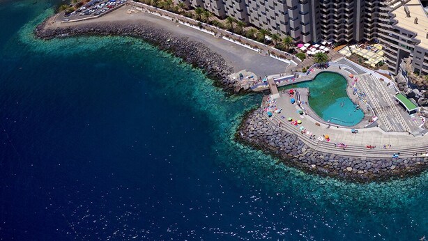Luftaufnahme eines Küstenresorts mit Schwimmbad, Parkplatz und Hochhäusern.