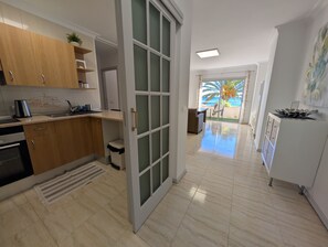 Une cuisine moderne avec des meubles en bois, une machine à café et une vue sur la mer par une porte vitrée.