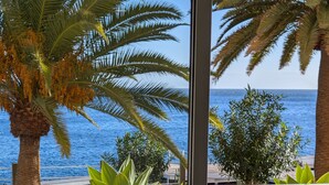 Ein Balkon mit Korbmöbeln, einem kleinen Tisch und Blick auf das Meer und Palmen.
