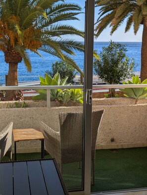 Un balcon agrémenté de meubles en osier, d’une petite table et offrant une vue sur la mer et les palmiers.
