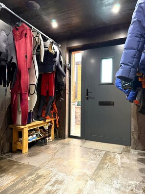 Ein Lagerraum mit Regalen für diverse Wintersportausrüstung, einer Tür nach draußen und einem Holzregal mit Schuhen.