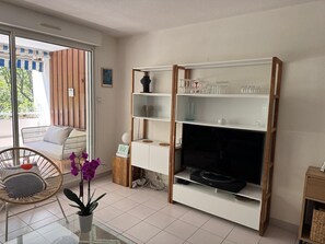 Ein Wohnzimmer mit einer Couch, einem Sessel, einer TV-Konsole mit Regalen und einer Zimmerpflanze.
