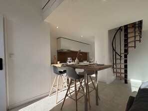Een moderne keuken met witte kasten, een eettafel met stoelen en een spiltrap.