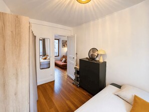 A bedroom with a bed, a dresser, a mirror, and a door leading to another room. - Charming, bright, quiet 16th arrondissement flat (Paris)