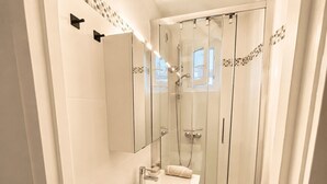 Ein modernes Badezimmer mit einer Duschkabine, einem Waschtisch mit Spiegel und einem Handtuchhalter.