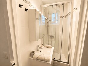 A modern bathroom with a glass-enclosed shower, a vanity with a mirror, and a towel rack. - Charming, bright, quiet 16th arrondissement flat (Paris)