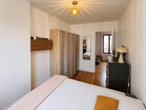 A bedroom with a bed, a bedside table, a lamp, a mirror, and a door leading to another room. - Charming, bright, quiet 16th arrondissement flat (Paris)