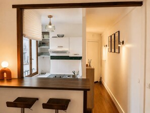 A modern kitchen with white cabinets, a green backsplash, and a hanging light fixture. - Charming, bright, quiet 16th arrondissement flat (Paris)
