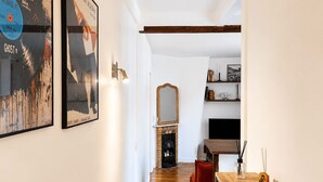 Ein Flur mit Holzboden, einem roten Stuhl, einem Holztisch mit weißer Schüssel, einem Spiegel und gerahmten Kunstwerken an der Wand.