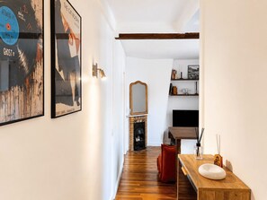 A hallway with a wooden floor, a red chair, a wooden table with a white bowl, a mirror, and framed artwork on the wall. - Charming, bright, quiet 16th arrondissement flat (Paris)