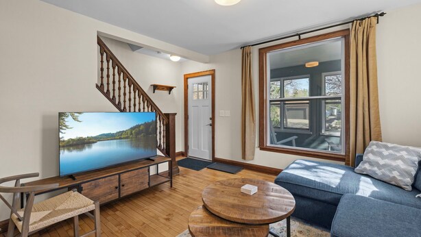 Un salon avec un téléviseur, un escalier en bois et une grande fenêtre avec des rideaux.